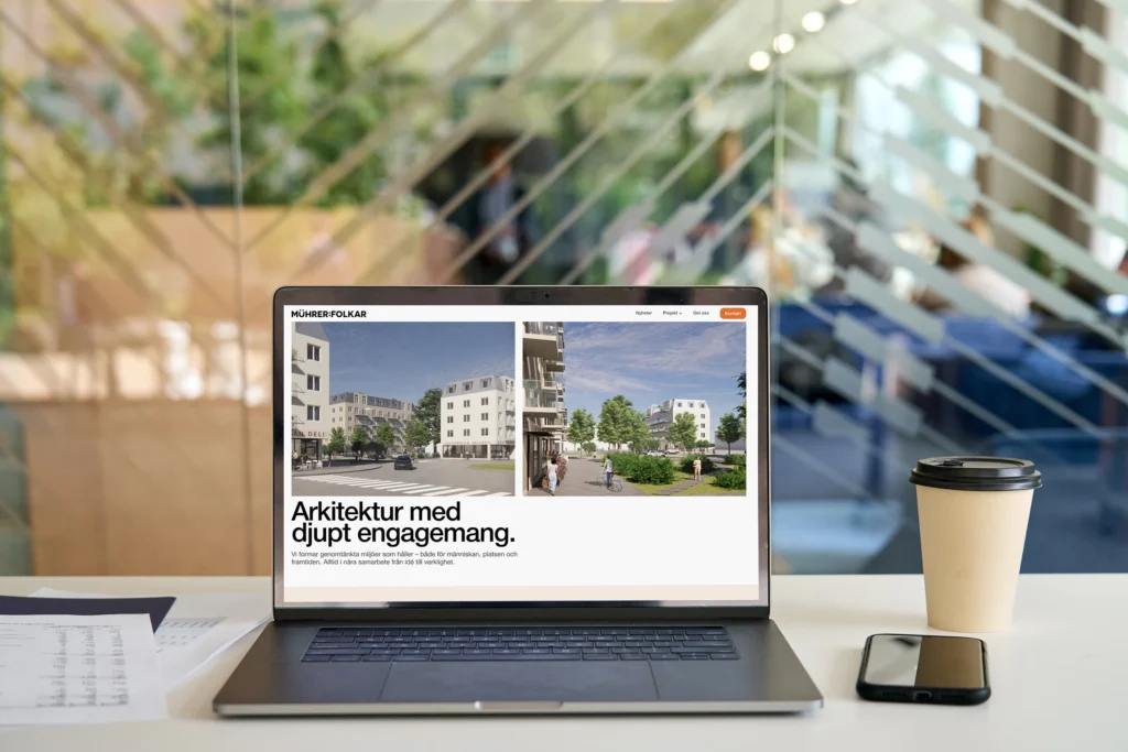 Hemsida för Muhrer Folkar som syns på en laptopskärm på ett vitt bord med kaffekopp bredvid