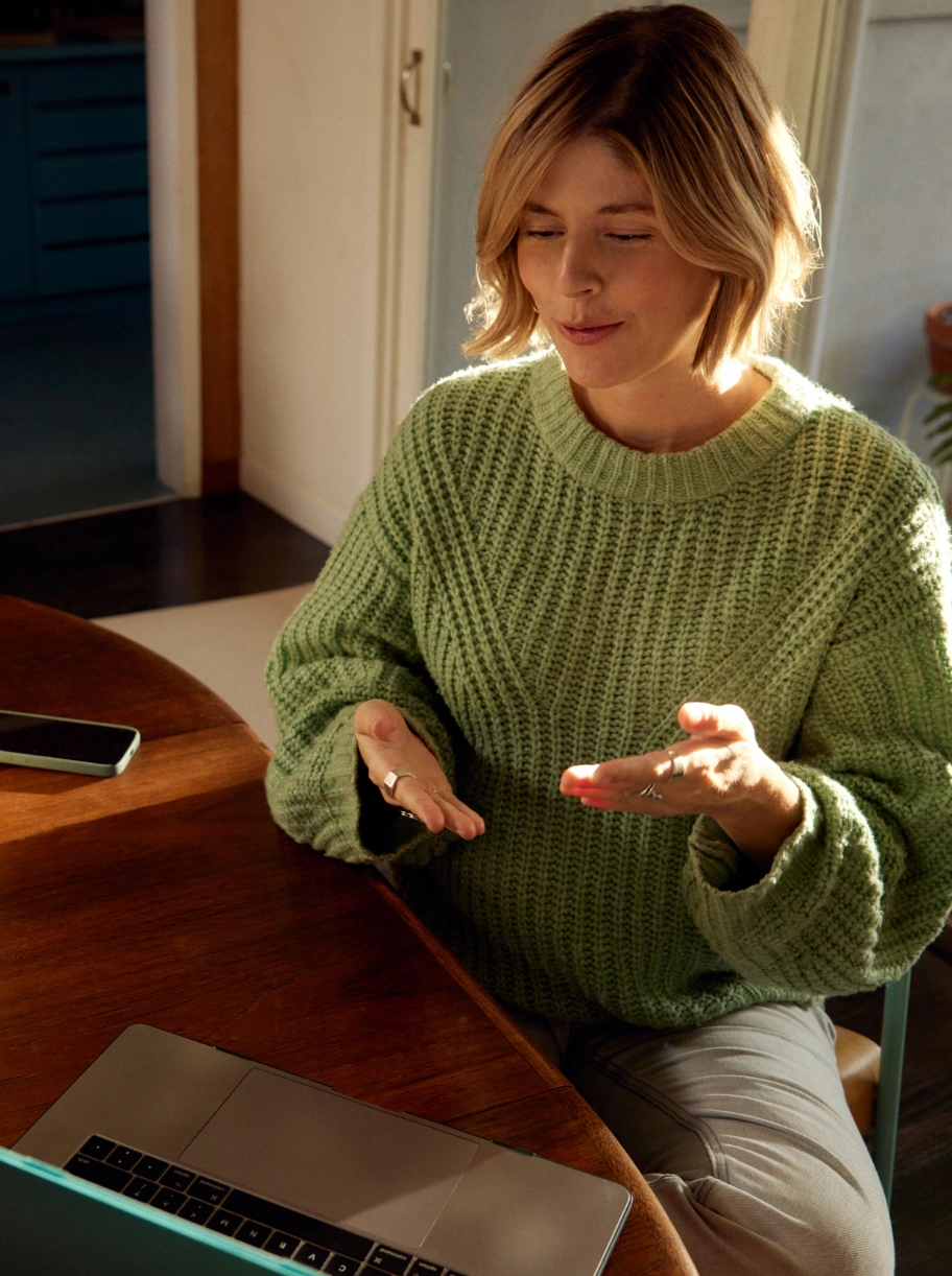 Blond kvinna i grön jumper som gestikulerar om varumärke framför en laptop gällande varumärkesstrategi för företag